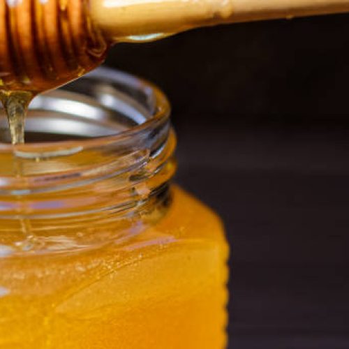 Honey in small glass jar with dipper. Black background. Close-up. Copy space
